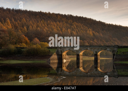 Vue panoramique du pont de la route d'arches ensoleillée & Woodland, reflétée dans l'eau calme de Lindley Wood - près de Otley, North Yorkshire, Angleterre, Royaume-Uni. Banque D'Images