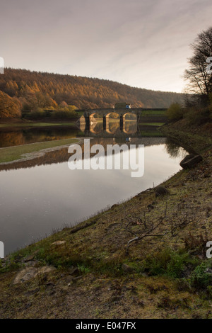 Vue panoramique du pont de la route d'arches ensoleillée & Woodland, reflétée dans l'eau calme de Lindley Wood - près de Otley, North Yorkshire, Angleterre, Royaume-Uni. Banque D'Images