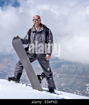 Male snowboarder dans les montagnes, debout sur le sommet de la montagne et tenant en mains, snowboard sport d'hiver Banque D'Images