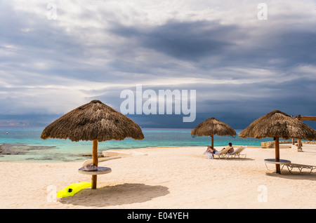 Des parasols en chaume sur une plage sous ciel nuageux. Cozumel, Mexique. Banque D'Images