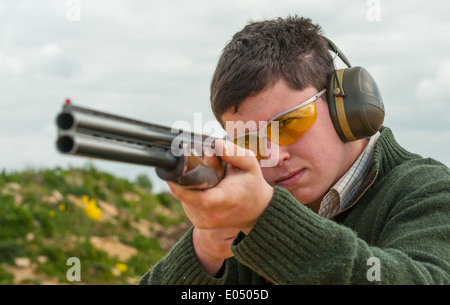 Jeune homme avec un pistolet à grenaille et sous un tir au pigeon d'argile sol Banque D'Images