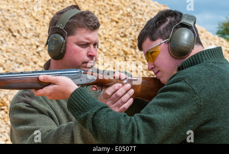 Jeune homme avec un pistolet à grenaille et sous un tir au pigeon d'argile sol coachés Banque D'Images