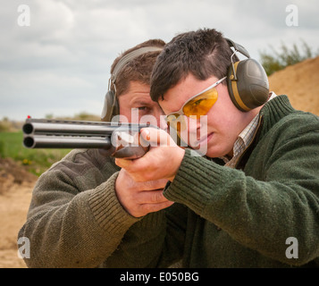 Jeune homme avec un pistolet à grenaille et sous un tir au pigeon d'argile sol coachés Banque D'Images