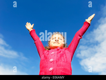 Petite fille lève ses mains vers le soleil sur fond de ciel bleu. Banque D'Images