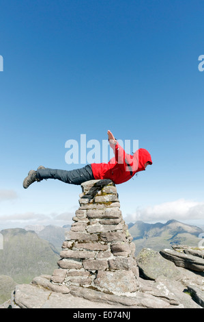 Un hillwalker dans une veste rouge faisant semblant d'être superman, battant sur le cairn du sommet de Beinn Alligin en Ecosse, Torridon Banque D'Images