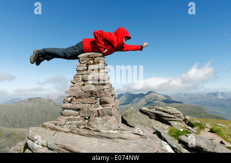 Un hillwalker dans une veste rouge faisant semblant d'être superman, battant sur le cairn du sommet de Beinn Alligin en Ecosse, Torridon Banque D'Images