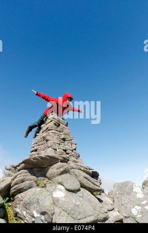 Un hillwalker dans une veste rouge faisant semblant d'être superman, battant sur le cairn du sommet de Beinn Alligin en Ecosse, Torridon Banque D'Images