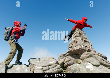 Un hillwalker dans une veste rouge faisant semblant d'être superman, battant sur le cairn du sommet de Beinn Alligin en Ecosse, Torridon Banque D'Images