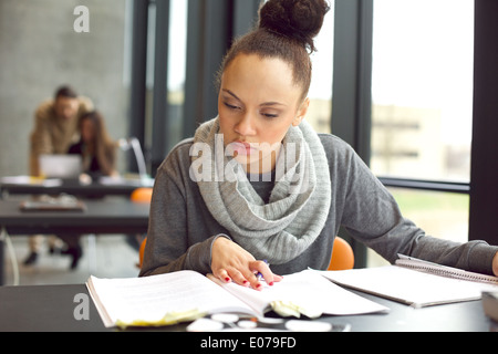 Élève de lire un livre pour trouver de l'information. Young african american woman sitting at table faisant des affectations. Banque D'Images