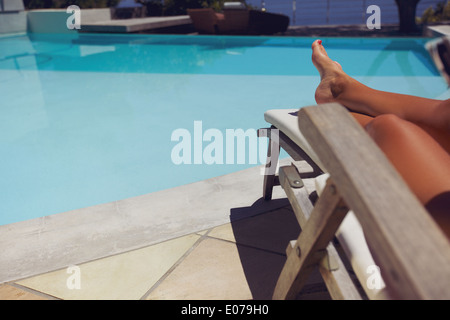 Jeune femme se détendre sur une chaise longue en piscine. Jambes de femmes assis sur une chaise en prenant le soleil. Banque D'Images