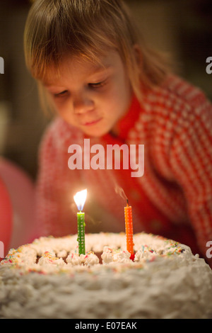 Little girl blowing out birthday candles on cake Banque D'Images