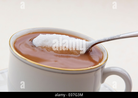 L'ajout d'une cuillerée de sucre blanc granulé dans d'une tasse de thé dans une tasse de Chine blanc. En Angleterre, Royaume-Uni, Angleterre Banque D'Images