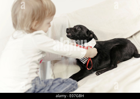 Petite fille jouant avec le chien sur un canapé Banque D'Images