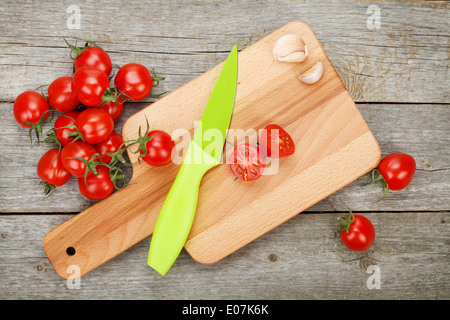 Les tomates cerise avec un couteau sur une planche à découper sur fond de table en bois Banque D'Images