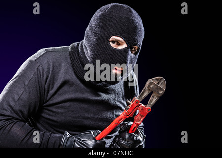 Un cambrioleur portant un énorme holding balaclava un coupe-fil sur fond noir Banque D'Images