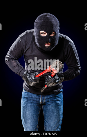 Un cambrioleur portant un énorme holding balaclava un coupe-fil sur fond noir Banque D'Images