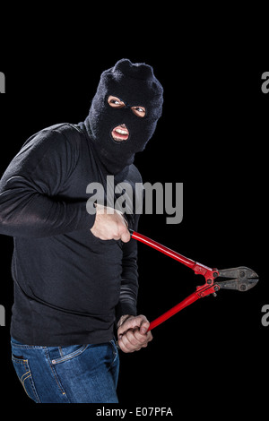 Un cambrioleur portant un énorme holding balaclava un coupe-fil sur fond noir Banque D'Images