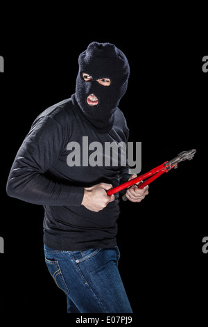 Un cambrioleur portant un énorme holding balaclava un coupe-fil sur fond noir Banque D'Images