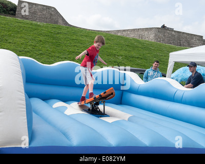 Un jeune garçon monte un simulateur de surf lors d'une fête d'été Banque D'Images