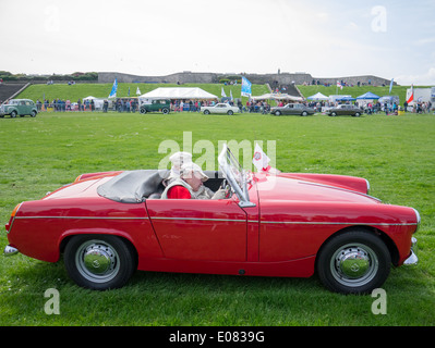 Un homme conduisant un rouge 1962 MG Midget Mk1 avec une passagère Banque D'Images