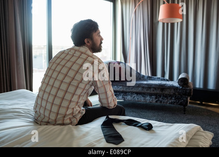 Vue arrière du businessman sitting on bed in hotel room Banque D'Images