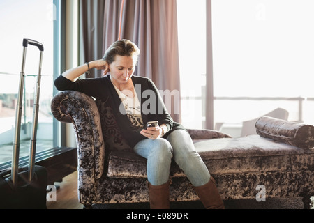 Businesswoman using mobile phone on chaise longue dans la chambre d'hôtel Banque D'Images