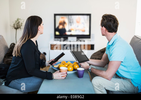 Vue latérale du couple watching TV alors que le café à la maison Banque D'Images