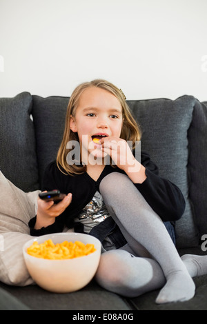 Fille de manger des collations en regardant la télévision sur un canapé à la maison Banque D'Images