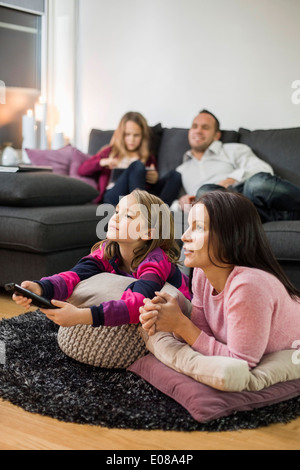 Mère et fille regarder la TV sur le plancher avec la famille en arrière-plan Banque D'Images