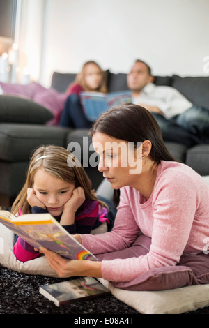 Mère et fille histoire lecture livre sur marbre avec la famille en arrière-plan Banque D'Images