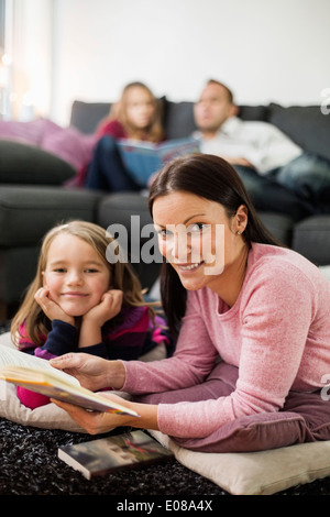 Portrait of happy mother and daughter with story book in living room Banque D'Images