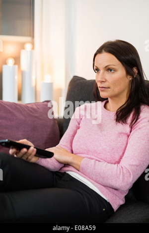 Mid adult woman watching TV on sofa at home Banque D'Images