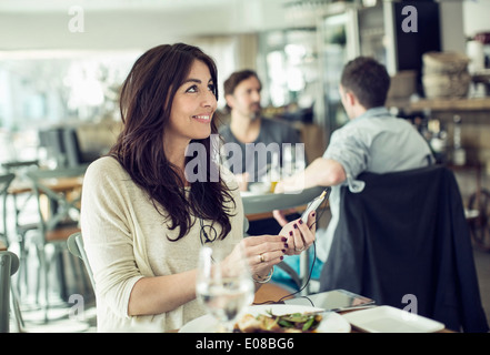 Smiling businesswoman holding mobile phone in restaurant Banque D'Images