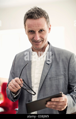 Portrait of businessman holding glasses and digital tablet in office Banque D'Images