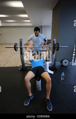 Homme soulevant des poids dans la salle de sport avec l'aide d'un détacheur Banque D'Images