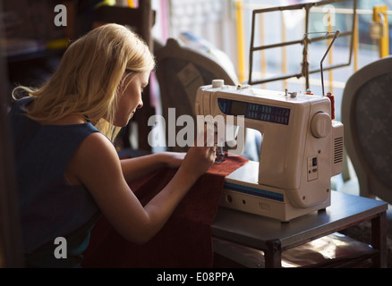 Vue latérale du designer de mode féminine à l'aide de machine à coudre dans studio Banque D'Images