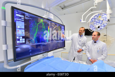 Jena, Allemagne. 06 mai, 2014. Directeur du Centre de radiologie Ulf Teichgraeber (L) et médecin principal René Aschenbach regardez le nouveau système d'angiographie sur un employé de l'hôpital à l'institut de radiologie diagnostique et interventionnelle (IDIR) à l'Hôpital universitaire de Jena, Allemagne, 06 mai 2014. C'est le premier hôpital en allemand à l'angiographie pour utiliser les soins aux patients. Un bras robotique flexible se déplace autour du patient permettant d'organes et les vaisseaux sanguins d'être vu plus facilement et plus rapidement à partir de différents angles. Photo : MARTIN SCHUTT/dpa/Alamy Live News Banque D'Images