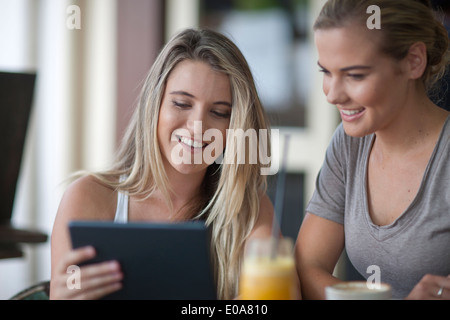 Deux jeunes femmes adultes friends looking at digital tablet in cafe Banque D'Images