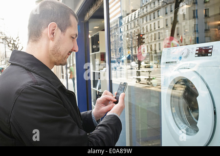 Mid adult man checking out lave linge dans shop using smartphone Banque D'Images