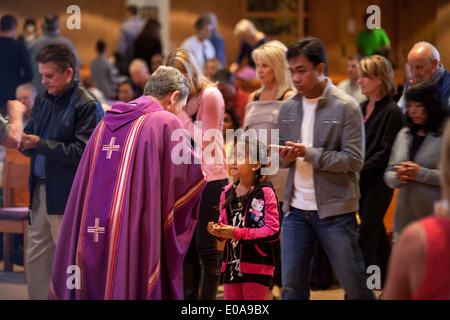 Lors d'une église catholique à Laguna Niguel, CA, a purple robed priest accueille un jeune paroissien hispanique au cours de l'offrande de la communion l'hôte à la fin de la messe. Banque D'Images