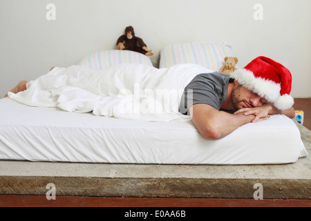 Mid adult man in santa hat endormi dans le lit Banque D'Images