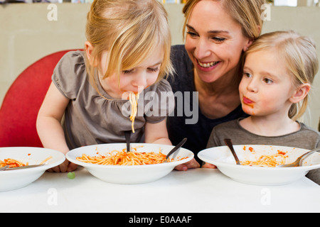 Mid adult mère mange du spaghetti avec ses deux jeunes filles Banque D'Images