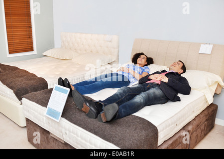 Couple lying on bed in furniture shop showroom Banque D'Images