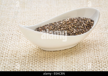 Les graines de chia (Salvia hispanica) dans un petit bol blanc toile de jute contre Banque D'Images