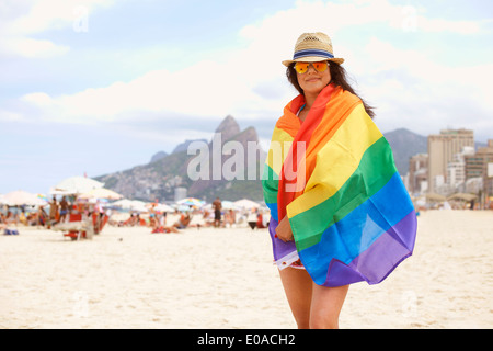 Portrait of mature femme enveloppée dans un drapeau multicolore, Ipanema beach, Rio de Janeiro, Brésil Banque D'Images