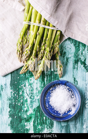 Bande de jeunes asperges vertes avec une plaque en céramique de sel de mer sur table en bois vert. Vue d'en haut. Banque D'Images