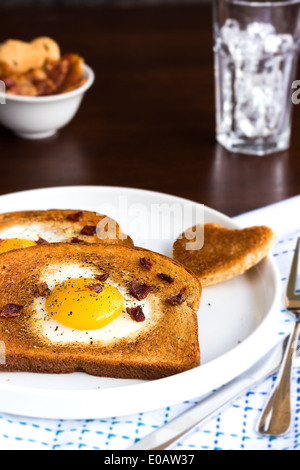 Frit oeufs dans une découpe en forme de coeur toast parsemés de miettes de bacon, de poivre concassé et de thym Banque D'Images