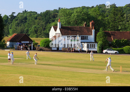 Les équipes locales de jouer un match de cricket sur un village vert en face de Barley Mow pub sur une soirée d'été. Tilford Surrey England UK Banque D'Images