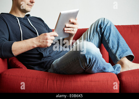 Mid adult man relaxing on sofa looking at digital tablet Banque D'Images