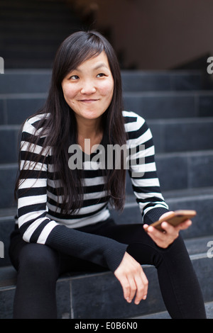 Mid adult woman sitting on steps holding smartphone Banque D'Images